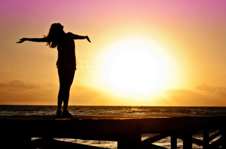 Silhouette d'une femme sur un ponton les bras ouverts vers l'horizon face au soleil, représentant sa confiance en soi.